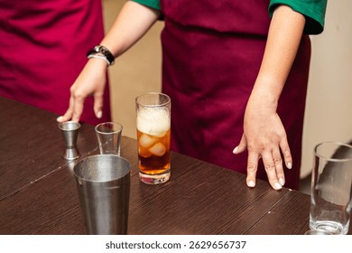 A cocktail mixing session in progress, featuring bartenders in aprons preparing a chilled drink with ice and bar tools.