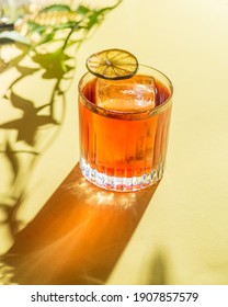 Cocktail in einem alten Modeglas auf Laub-Hintergrund, Schatten von der Sonne. gelber Hintergrund