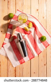 Cocktail Shaker With An Iced Martini Cocktail And Fresh Lemon And Lime On A Striped Red And White Napkin On A Rustic Wooden Table Outdoors In Sunshine