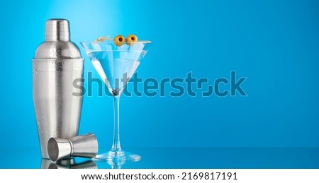 Cocktail shaker and martini cocktail on blue background with copy space