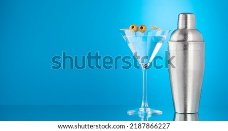 Cocktail shaker and martini cocktail on blue background with copy space