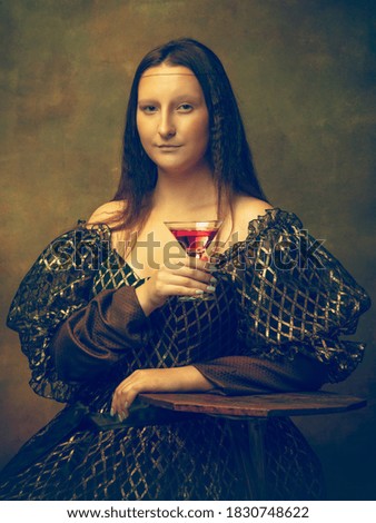 Cocktail time. Young woman as Mona Lisa, La Gioconda isolated on dark green background. Retro style, comparison of eras concept. Beautiful female model like classic historical character, old-fashioned