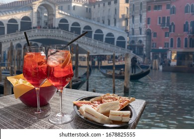 Cocktail for two prepared with straws and lemon and a bowl of snacks. In the background the Rialto Bridge in Venice.