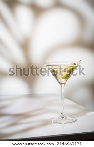 Cocktail vodka martini with green olives on light background with bright beautiful shadows