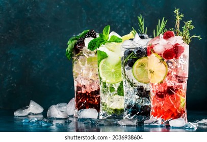 Cocktails drinks. Classic alcoholic long drink or mocktail highballs with berries, lime, herbs and ice on blue background