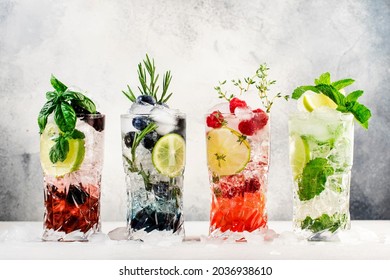 Cocktails drinks. Classic alcoholic long drink or mocktail highballs with berries, lime, herbs and ice on gray background