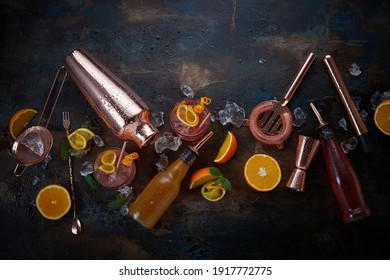 Cocktails or pub flat lay still life with copper bar equipment, chilled alcoholic beverages in glasses and sliced fresh oranges for garnishes scattered on a dark background