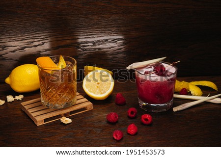 Cocktails in rocks glasses on wooden background. Raspberry gin and old fashioned 