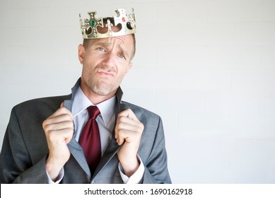 Cocky businessman wearing golden jeweled crown popping his collar with an arrogant expression