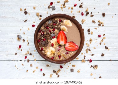 cocoa banana protein smoothie bowl with chocolate granola, strawberry and pomegranate seeds. top view. healthy breakfast