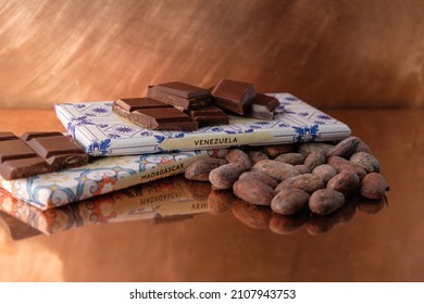 Cocoa beans and chocolate on a copper background. Chocolate with the inscription Madagascar, Venezuela. Reflection.