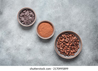 Cocoa Beans, Cocoa Powder And Chocolate In Bowls On Grunge Gray Background. View From Above.