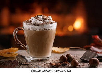 Cocoa with marshmallows and chocolate in a glass mug on a wooden table near a burning fireplace - Powered by Shutterstock