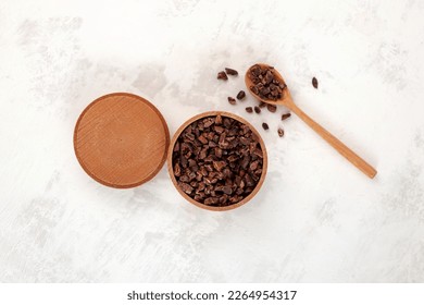 Cocoa nibs in wooden bowl with spoon, top view. Sugar-free product, Natural antidepressant. Cacao nibs are often added to cereals, smoothies, desserts, drinks, raw food and vegan dishes.