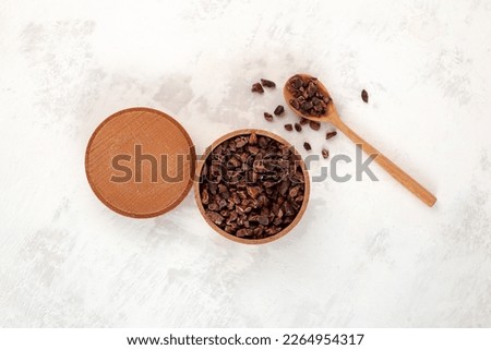 Cocoa nibs in wooden bowl with spoon, top view. Sugar-free product, Natural antidepressant. Cacao nibs are often added to cereals, smoothies, desserts, drinks, raw food and vegan dishes.