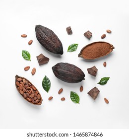 Cocoa pods with beans, powder and chocolate pieces on white background, top view