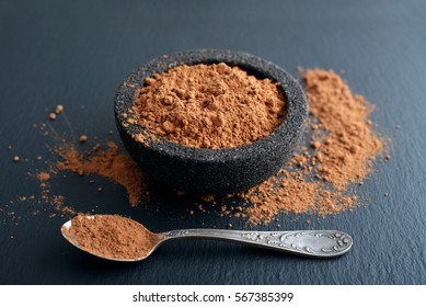 Cocoa Powder In A Bowl With Spoon On The Black Slate Background