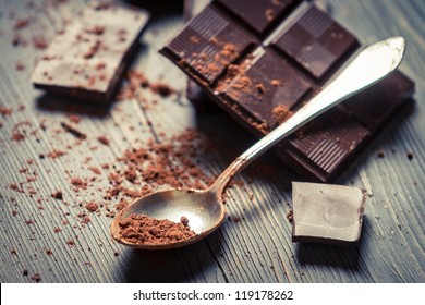 Cocoa Powder On Spoon And Dark Chocolate Background