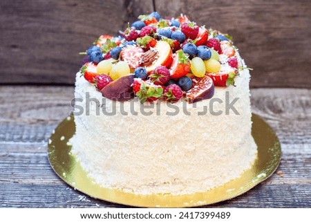Coconut cake with a pile of fresh peaches, apples, raspberries, blueberries and nuts on wooden background