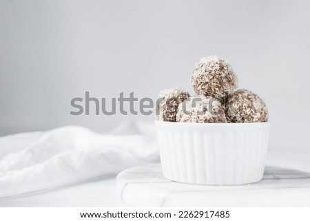 Coconut and chocolate truffles in white ramekin, homemade chocolate bonbons on white background, desiccated coconut coated truffles