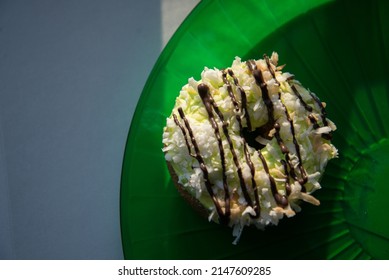 Coconut Donut With A Chocolate Drizzle And Green Icing On A Green Plate