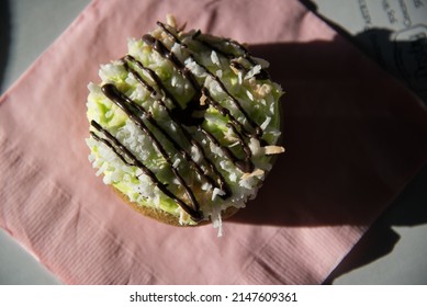 Coconut Donut With A Chocolate Drizzle And Green Icing On A Green Plate