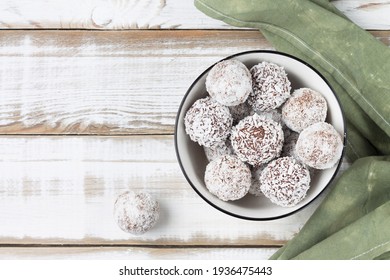 Coconut energy balls in a white cup on a light wooden background. Top view.
