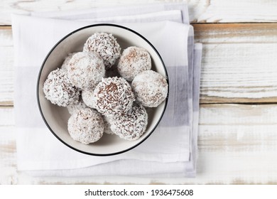 Coconut energy balls in a white cup on a light wooden background.
