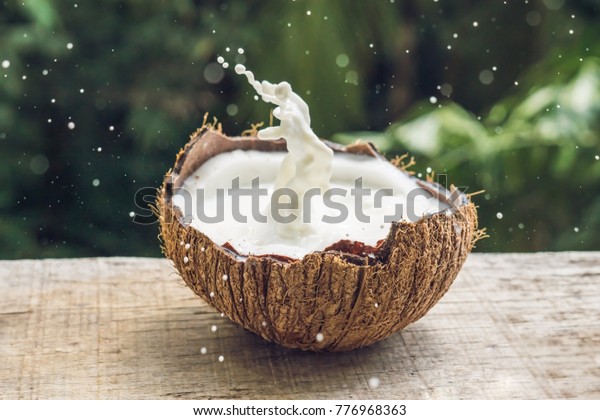 Coconut fruit and milk splash inside it on a\
background of a palm\
tree.