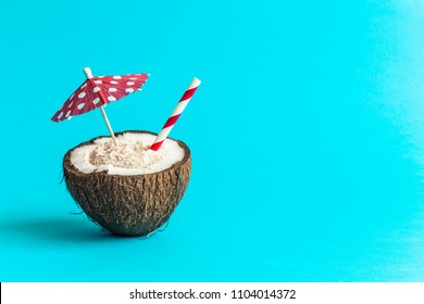 Coconut Full Of Sand With Red Polka Paper Cocktail Umbrella And Drinking Straw Summer Vacation Tropical Minimal Creative Concept.