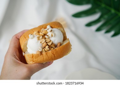 Coconut ice cream with bread. Hand holding a soft bread topped with two scoop of coconut sorbet ice cream and peanut. A famous Thailand street food.