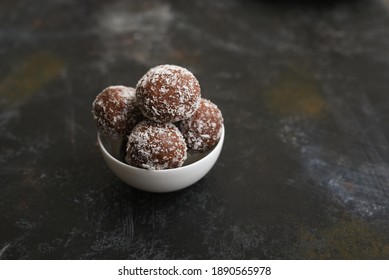 Coconut Ladoo, chocolate coconut balls Indian sweet recipe on banana leaf plate on white background. Popular sweet snack of Kerala Tamil Nadu South India. Top view of Indian veg snack food.