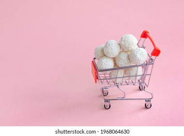 coconut round candies in a mini shopping basket, isolate on a pinc background. Supermarket shopping concept. full cart of sweets. High quality photo