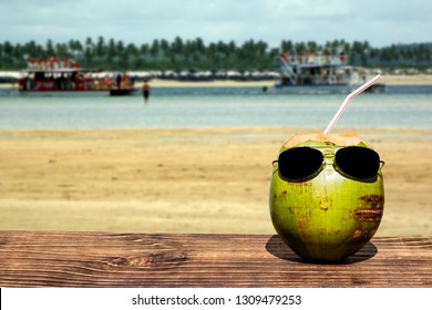 Coconut with sunglasses over wood, blurred beach background, space for text - Powered by Shutterstock