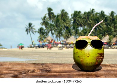 Coconut with sunglasses over wood, blurred beach background, space for text - Powered by Shutterstock