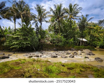 Coconut trees line the riverbank. Lush greenery covers the surrounding hills, and small village can be seen in the distance. The river is filled with rocks and rapids, creating a dynamic and energetic - Powered by Shutterstock