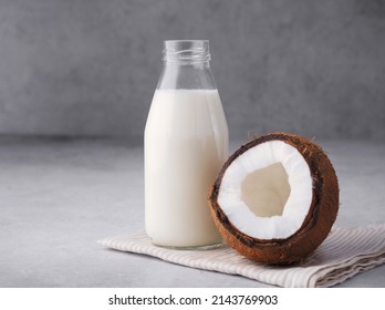 Coconut Vegan Milk Is Non Dairy Products In A Bottle With A Place To Copy On A Gray Concrete Background. Glass Bottle Of Milk Or Yogurt With Coconut Chips Aside. Concept Of Healthy Eating. Close Up.