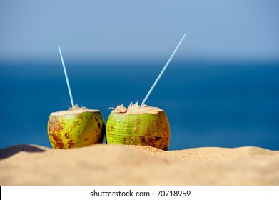 Coconuts with drinking straw on the sand at the sea
