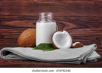 Coconuts and a jar of coconut milk on a gray piece of cloth on a dark wooden background.  Cut tasty coconuts and a bottle full of delicious fresh milk. Beautiful nutritious nuts. - Powered by Shutterstock