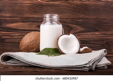 Coconuts and a jar of coconut milk on a gray piece of cloth on a dark wooden background. Cut tasty coconuts and a bottle full of delicious fresh milk. Beautiful nutritious nuts. - Powered by Shutterstock