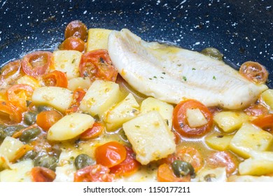 cod cooked in a pan, with tomato, potatoes and capers