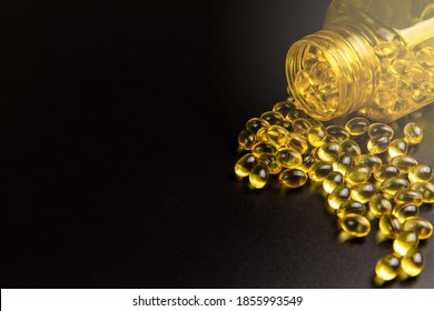 Cod liver oil omega 3 gel capsules on black background. Vitamin D and golden Omega 3 pills for healthy diet nutrition. Influenza prevention.