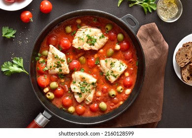 Cod stew with chickpeas, cherry tomatoes and olives in cooking pan over dark stone background. Top view, flat lay Stock Photo