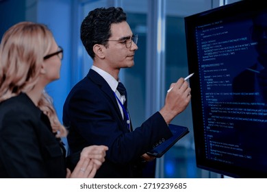 Code breakthrough achieved. Smiling senior developer points to a successful code segment on screen, sharing the solution with his colleague during a late night pair programming session.