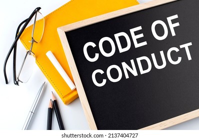 CODE OF CONDUCT text on a blackboard with notepad , pen, pencil