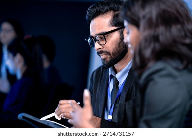 Code deep dive briefing. Experienced male developer explains software architecture or complex algorithm to female engineer with code visible on screen in background tech hub.