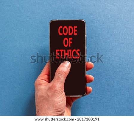 Code of ethics words symbol. Concept words Code of ethics on beautiful black mobile phone screen. Beautiful blue background. Businessman hand. Business Code of ethics concept. Copy space.