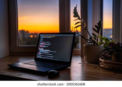 The code is on a laptop on a wooden table in front of the window  in the dark with a view of the lights of the night city, color lighting in the room, home decor	