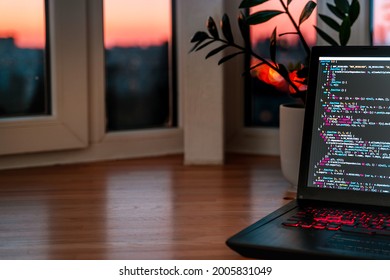 The code is on a laptop on a wooden table in front of the window  in the dark with a view of the lights of the night city, color lighting in the room, home decor	