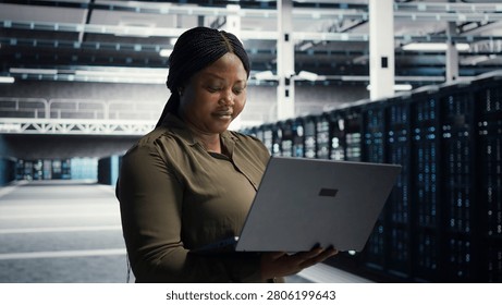 Coder in server facility working with notebook computer to update systems for increased stability. IT professional in server environment setting up infrastructure with notebook for optimum performanc.
